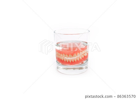 A denture in a glass of water. Dental prosthesis care. Full removable plastic denture of the jaws. Two acrylic dentures. Upper and lower jaws with fake teeth. Dentures or false teeth, close-up. A denture in a glass of water. Dental prosthesis care. Full removable plastic denture of the jaws. Two acrylic dentures. Upper and lower jaws with fake teeth. Dentures or false teeth, close-up. 86363570