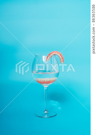 A denture in a glass of water. Dental prosthesis care. Full removable plastic denture of the jaws. Two acrylic dentures. Upper and lower jaws with fake teeth. Dentures or false teeth, close-up. 86363586