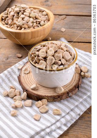 Dry raw cicerchia or indian pea on a ceramic bowl with napkin on wooden background, close up 86363703