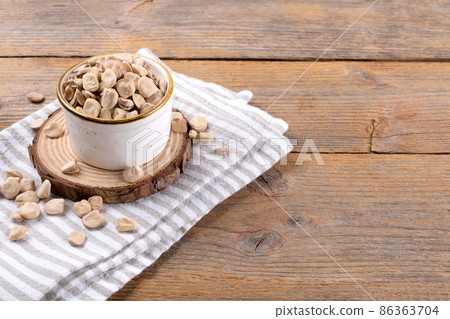 Dry raw cicerchia or indian pea on a ceramic bowl with napkin on wooden background, copy space 86363704