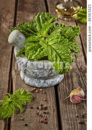 Stone mortar with curly basil and condiments on wooden table Stone mortar with curly basil and condiments on wooden table 86363825