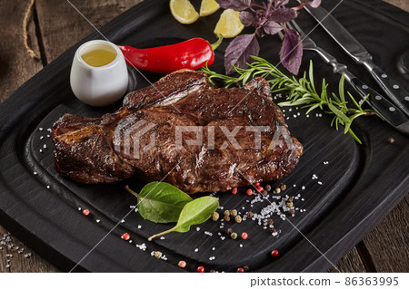 Closeup of roasted veal steak with condiments on serving board with cutlery Closeup of roasted veal steak with condiments on serving board with cutlery 86363995