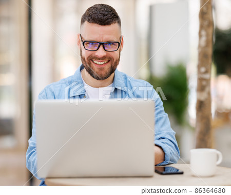 Happy young male businessman sitting in front of laptop outside working and having video conferencing online 86364680