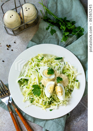 Healthy salad. Vegan salad with cabbage, eggs, cucumber, coriander and mayonnaise-mustard dressing on a light stone or slate table. 86365245