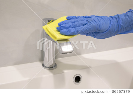 Person hand In blue glove cleaning silver basin mixer and white sink Person hand In blue glove cleaning silver basin mixer and white sink 86367579