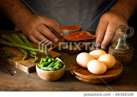 Green asparagus kept in men's Chef cook hands on wooden background. Green asparagus kept in men's Chef cook hands on wooden background. 86368106