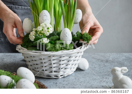 Woman make Easter floral composition with eggs, green moss and bunny. Woman make Easter floral composition with eggs, green moss and bunny. 86368187