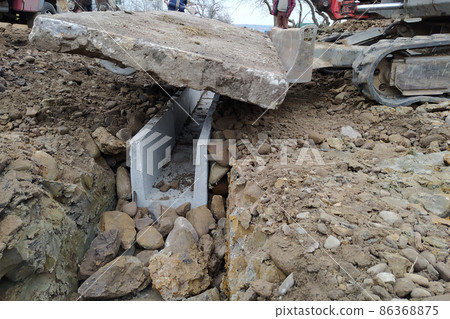 The excavator installs concrete trays for drainage of rainwater in rural areas, concrete products for drainage of water. The excavator installs concrete trays for drainage of rainwater in rural areas, concrete products for drainage of water. 86368875