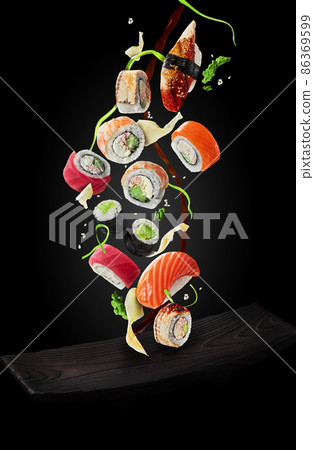 Sushi with garnishes and soy sauce hovering over plate on black background Sushi with garnishes and soy sauce hovering over plate on black background 86369599