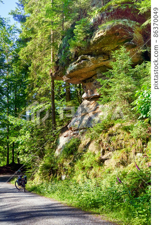 Sandstone cliff with an overhang on a bike path mi a bike parked during bike ride, horizontal stratification of sediments 86370049
