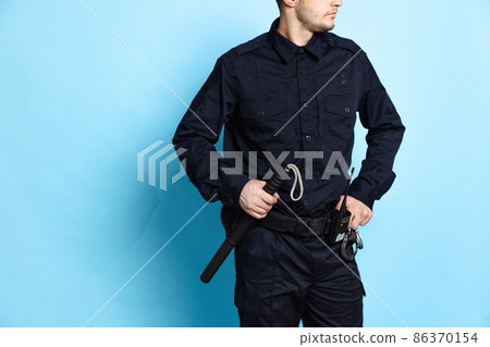 Cropped image of male policeman officer wearing black uniform with professional ammunition isolated on blue background. Cropped image of male policeman officer wearing black uniform with professional ammunition isolated on blue background. 86370154