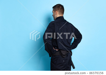 Back view of young man, policeman officer wearing black uniform isolated on blue background. Concept of job, caree, law and order. 86370156