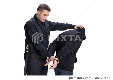 Young male policeman officer wearing black uniform with professional ammunition arrests a criminal isolated on white background. 86370167