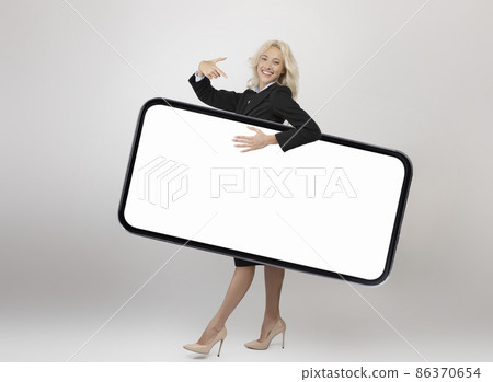 Full body length shot of happy businesswoman carrying big smartphone with blank screen and pointing at gadget screen 86370654