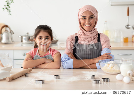 Baking Squad. Happy Islamic Mother And Little Daughter Cooking Pastry In Kitchen Baking Squad. Happy Islamic Mother And Little Daughter Cooking Pastry In Kitchen 86370657