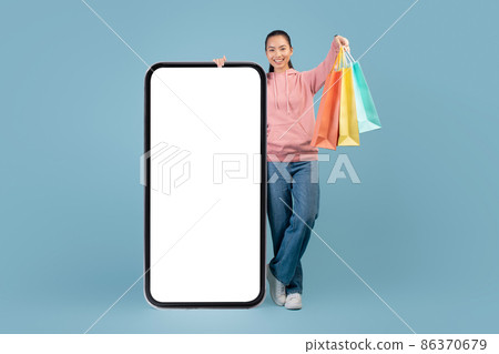 Positive chinese woman shopaholic with shopping bags and big smartphone Positive chinese woman shopaholic with shopping bags and big smartphone 86370679