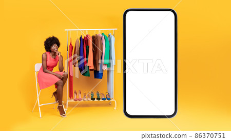 Black Woman Sitting Near Cellphone And Clothing Rack, Yellow Background Black Woman Sitting Near Cellphone And Clothing Rack, Yellow Background 86370751
