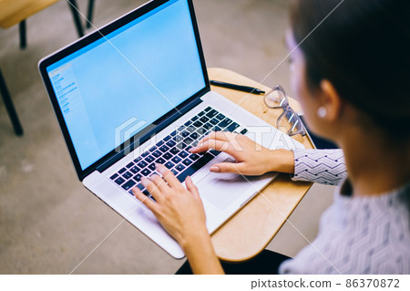 Unrecognizable female sitting at table and typing on laptop 86370872