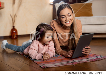 Smiling woman and girl using tablet at home Smiling woman and girl using tablet at home 86370996