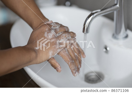 Handwashing concept. Young indian man washing hands with antibacterial soap under falling tap water in wash-basin 86371106