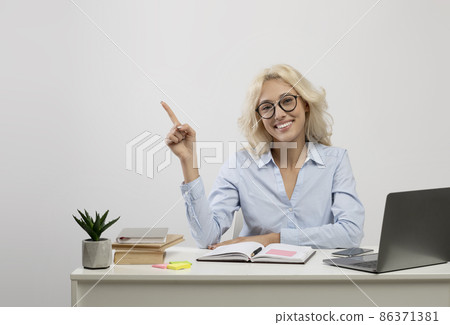 Happy young businesswoman sitting at workplace with pc laptop and pointing finger at free space on light background 86371381