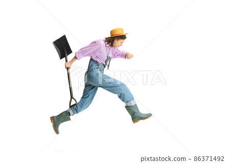 Dynamic portrait of young girl, female gardener in work uniform and gumboots running away isolated on white background. Concept of job, emotions, agronomy Dynamic portrait of young girl, female gardener in work uniform and gumboots running away isolated on white background. Concept of job, emotions, agronomy 86371492