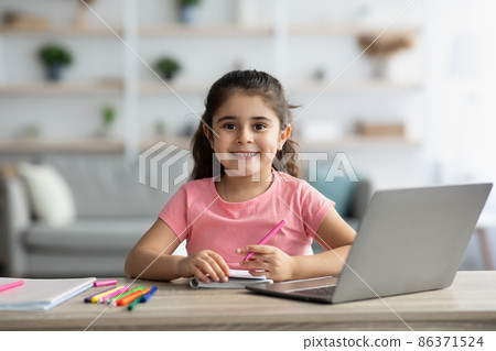 Cute Little Girl Sitting At Table With Laptop And Drawing In Notepad 86371524
