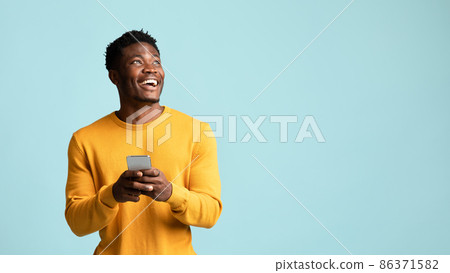 Cheerful black man using smartphone, looking at copy space Cheerful black man using smartphone, looking at copy space 86371582