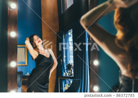 Sexy young woman in elegant cocktail silk black dress dancing and posing in mirror reflection in luxury interior. Fashionable and self-confident lady. Celebrity, superstar lifestyle. Selective focus Sexy young woman in elegant cocktail silk black dress dancing and posing in mirror reflection in luxury interior. Fashionable and self-confident lady. Celebrity, superstar lifestyle. Selective focus 86372785