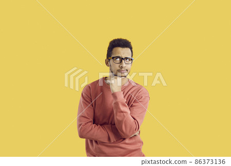 Hmm. Young student in glasses doubting something. Puzzled adult man in casual sweatshirt isolated on solid yellow background looking up and thinking hard about difficult question or future career plan 86373136