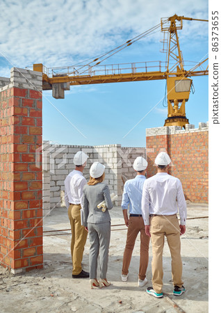 Four people in protective helmets inspecting the building area Four people in protective helmets inspecting the building area 86373655