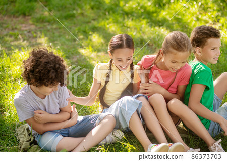 Smiling children sitting on grass in park Smiling children sitting on grass in park 86373703