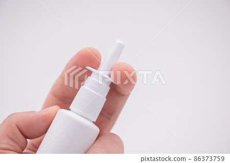 Holding nasal spray between fingers isolated on white background Holding nasal spray between fingers isolated on white background 86373759
