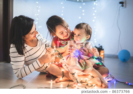 Mother with her daughters play with christmass lights Mother with her daughters play with christmass lights 86373766