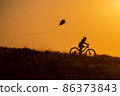 Silhouette of a child riding a bicycle with a kite in his hand 86373843