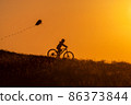 Silhouette of a child riding a bicycle with a kite in his hand 86373844