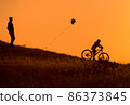Silhouette of a father and his child riding a bicycle with a kite in his hand 86373845