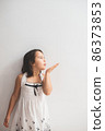Cute girl standing next to an white wall and blowing kisses 86373853