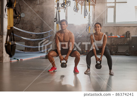 Male personal trainer training female client in gym Male personal trainer training female client in gym 86374241