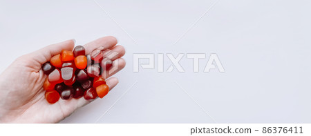 Group of red, orange and purple multivitamin gummies in the hand isolated on white background 86376411
