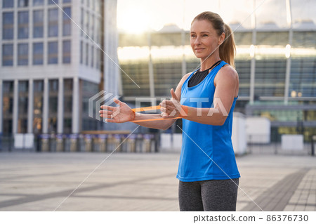 Beautiful sportive woman in sportswear, female trainer holding resistance band while standing outdoors, working out in the city Beautiful sportive woman in sportswear, female trainer holding resistance band while standing outdoors, working out in the city 86376730