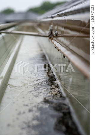 Selective focus on a section of residential guttering with hanger conveying water during a storm. Rain splatters and drops visible. 86377122
