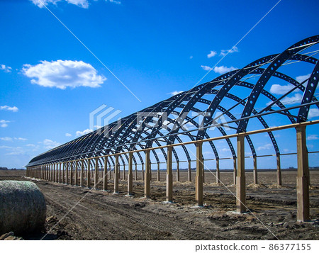 Frame and metal arches of a fabric covered hoop barn under construction. Frame and metal arches of a fabric covered hoop barn under construction. 86377155