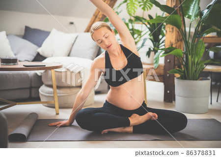 Young beautiful pregnant woman training yoga at home in her living room. Motherhood, pregnancy, healthy lifestyle and yoga concept Young beautiful pregnant woman training yoga at home in her living room. Motherhood, pregnancy, healthy lifestyle and yoga concept 86378831