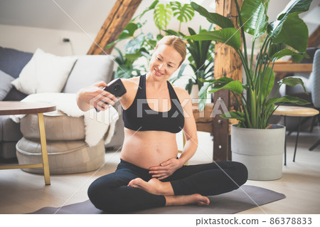 Young happy and cheerful beautiful pregnant woman taking selfie with her mobile phone while staying fit, sporty and active on her maternity leave. Motherhood, pregnancy, yoga concept. 86378833