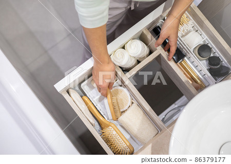 Top view of woman hands neatly organizing bathroom amenities and toiletries in drawer in bathroom. 86379177