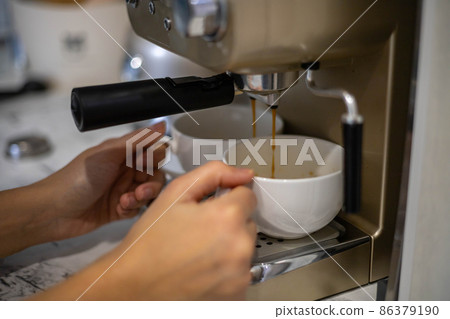 Female hands holding two white porcelain cups cooking fragrance aroma morning coffee in machine Female hands holding two white porcelain cups cooking fragrance aroma morning coffee in machine 86379190