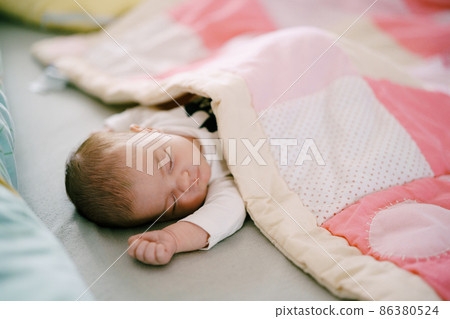 Baby sleeps on bed covered with pink patchwork quilt 86380524