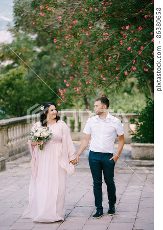 Bride in a pink dress with a bouquet holds the groom hand Bride in a pink dress with a bouquet holds the groom hand 86380658