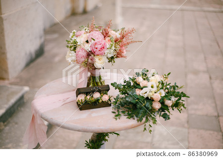 Bouquet in a vase with ribbons stands on the registration table next to a wooden box Bouquet in a vase with ribbons stands on the registration table next to a wooden box 86380969